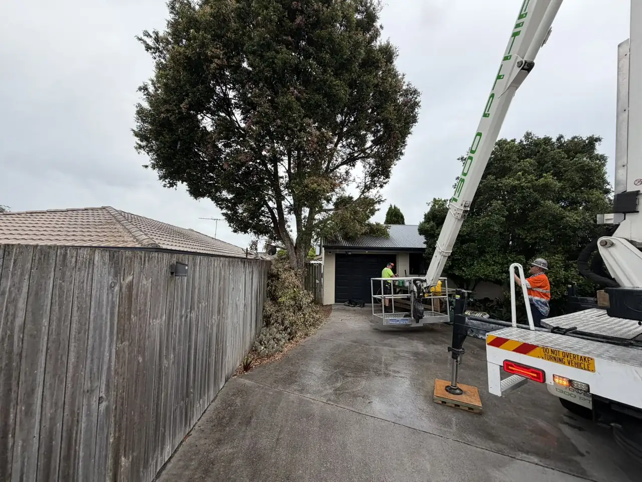 Spider lift and tipper truck set up on a driveway for a tree removal between a house and shed